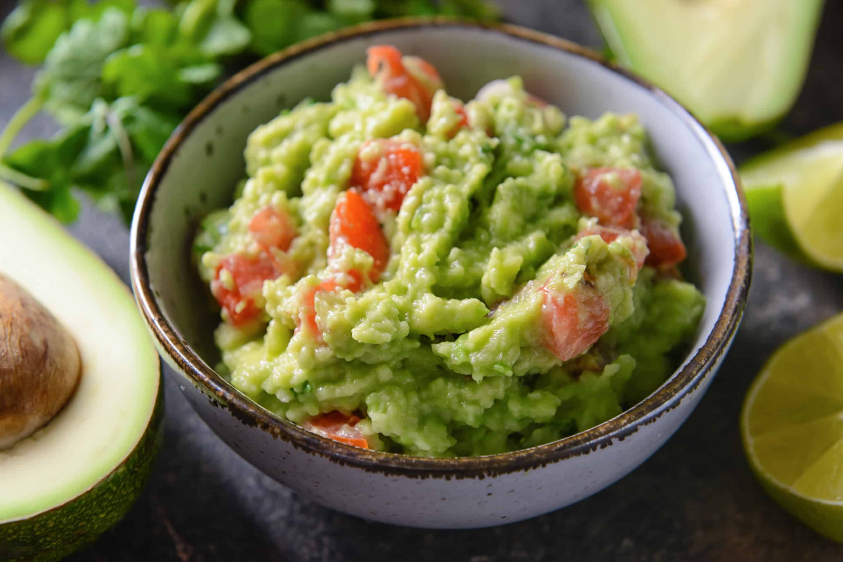 Bowl with tasty guacamole on dark background, closeup